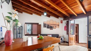 A kitchen with a wooden countertop, a vase with flowers, and a dining area with chairs and a sofa.