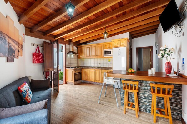 A kitchen with wooden cabinets, a microwave, and a refrigerator. There is a wooden ceiling with exposed beams and a hanging light fixture.