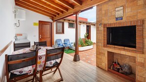 A covered patio with a table and chairs, a brick fireplace, and a door leading to an outdoor area.