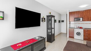 A modern living room with a flat-screen TV, a glass cabinet, a sofa, and a kitchen area with a washing machine. - Vacation Apartment 'Calipso Sun and Beach' with Sea View, Wi-Fi and Air Conditioning (Puertorico)