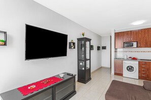 A modern living room with a flat-screen TV, a glass cabinet, a sofa, and a kitchen area with a washing machine. - Vacation Apartment 'Calipso Sun and Beach' with Sea View, Wi-Fi and Air Conditioning (Puertorico)