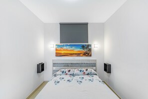 Un dormitorio con cama, un cuadro, un ventanal y dos altavoces integrados en la pared.