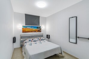 A bedroom with a bed, a painting, a window, a mirror, and a wall-mounted light fixture.