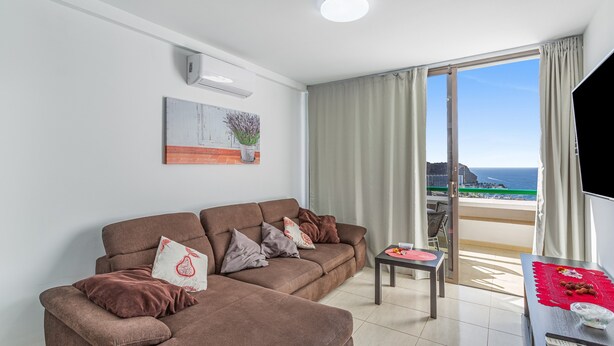 A living room with a sofa, a small table, and a view of the ocean. - Vacation Apartment 'Calipso Sun and Beach' with Sea View, Wi-Fi and Air Conditioning (Puertorico)
