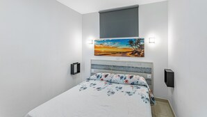 A bedroom with a bed, a painting, a window with a blind, and a wall-mounted light. - Vacation Apartment 'Calipso Sun and Beach' with Sea View, Wi-Fi and Air Conditioning (Puertorico)