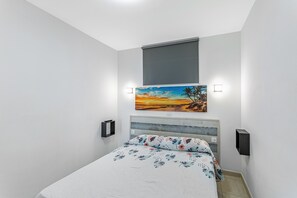 A bedroom with a bed, a painting, a window with a blind, and a wall-mounted light. - Vacation Apartment 'Calipso Sun and Beach' with Sea View, Wi-Fi and Air Conditioning (Puertorico)