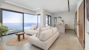 Een moderne woonkamer met een groot raam, een bank, een kleine tafel en een keukenhoek.