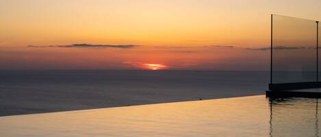 Een zonsondergang boven de oceaan met een heldere lucht, een zwembad en een glazen balustrade.
