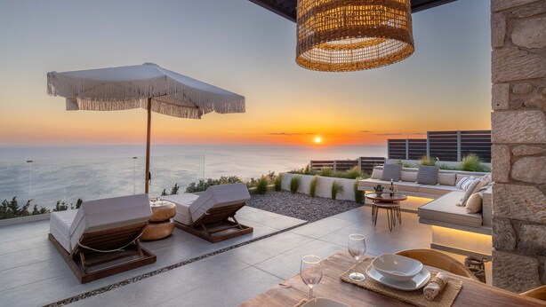 Een terras op het dak met uitzicht op een zonsondergang, ligbedden, een eettafel en een hanglamp.