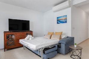 Um quarto com cama, televisão, penteadeira, quadro e pequena mesa com planta.