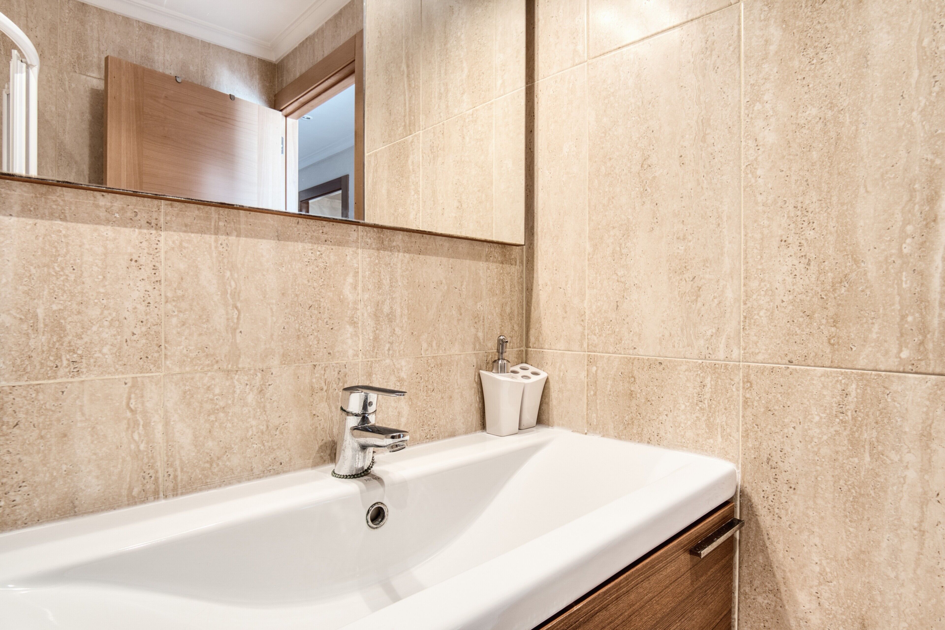 A bathroom with a white bathtub, a chrome faucet, and a wooden vanity.