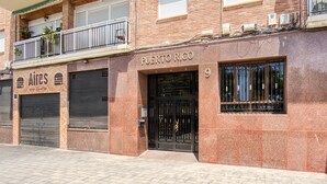 Um edifício com uma persiana fechada à esquerda, um letreiro com a inscrição 'PUERTO RICO' acima da porta e uma varanda com plantas.