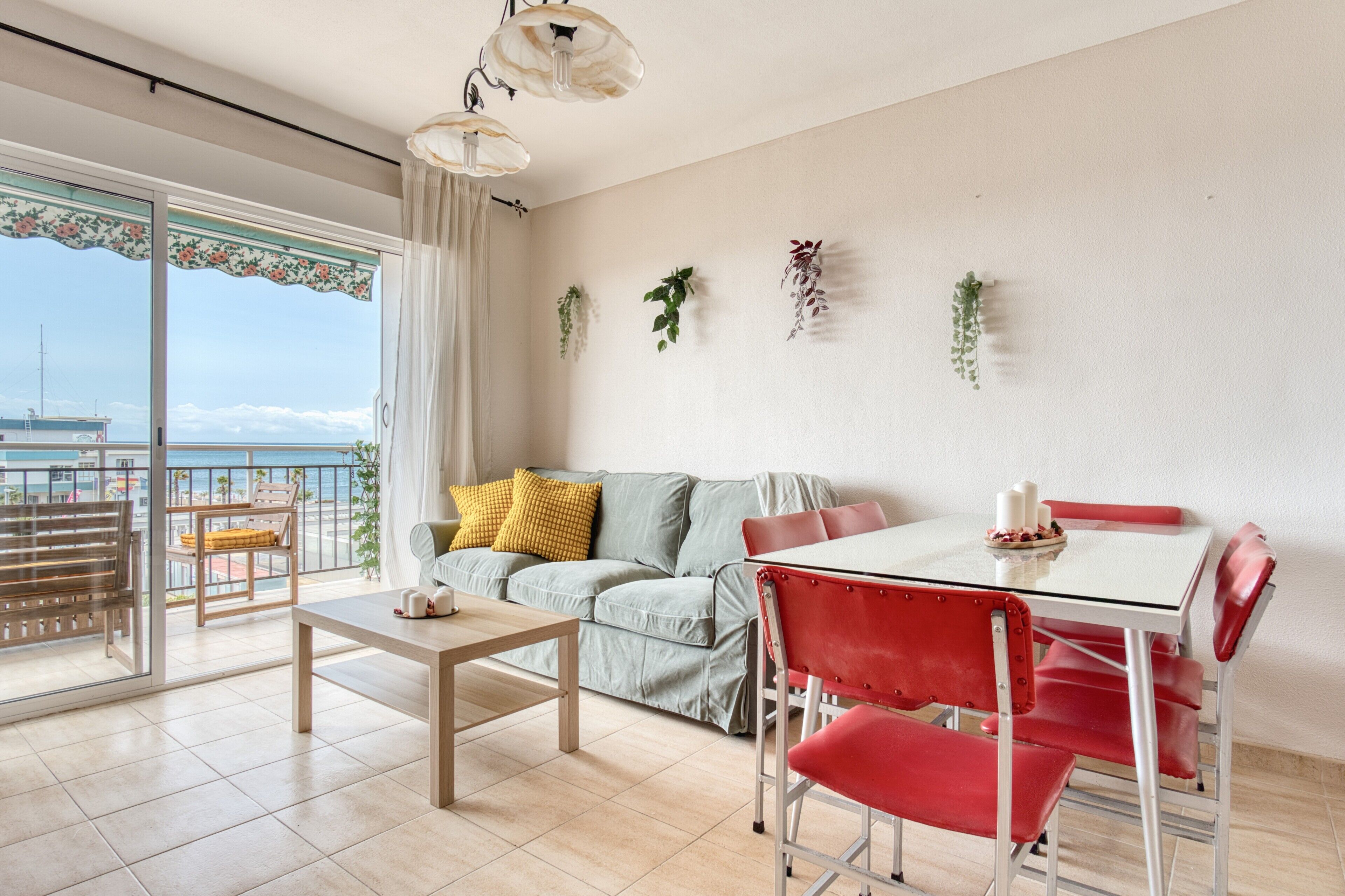 Un salon avec un canapé, une table à manger et des chaises, un balcon avec vue et des plantes suspendues au mur.