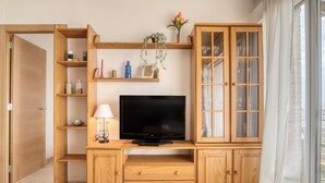 Uma sala de estar com televisão, armários de madeira, prateleiras e uma porta.
