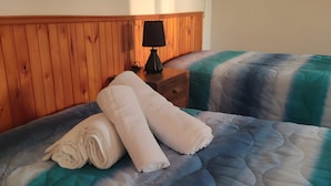 A bed with a quilt, a wooden headboard, a nightstand with a lamp, and a wall socket.