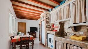 A compact kitchen with a washing machine, a dining area with a table and chairs, and a television in the background.