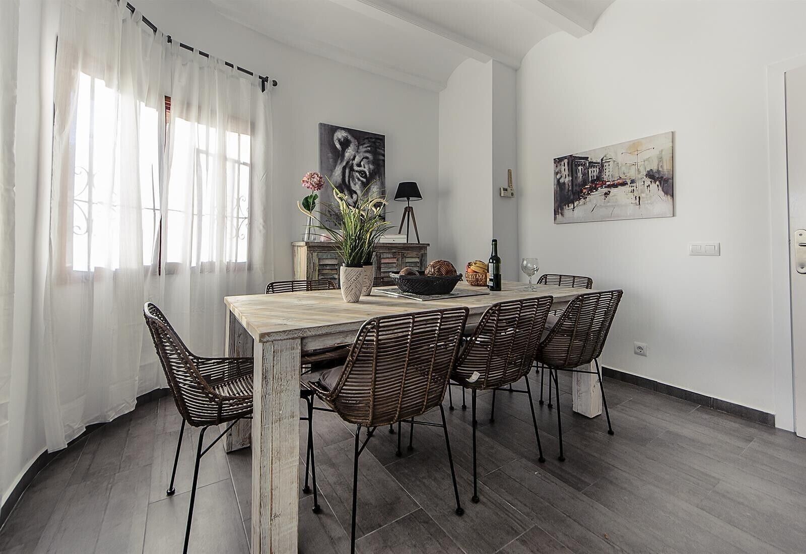 A dining area with a wooden table, wicker chairs, a potted plant, and artwork on the walls.
