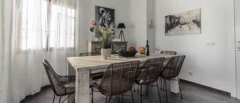 A dining area with a wooden table, wicker chairs, a potted plant, and artwork on the walls.