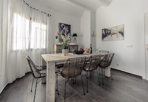 Un comedor con una mesa de madera, sillas de mimbre, una planta en maceta y obras de arte en las paredes.
