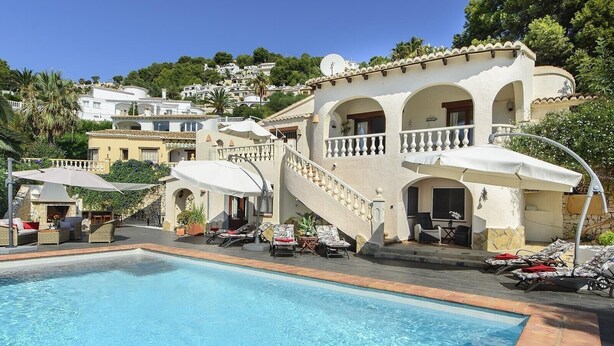 Un espace aménagé au bord de la piscine, comprenant une piscine, des chaises longues et un escalier menant à un bâtiment doté d’arcades et d’un balcon.