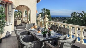 Un espace extérieur aménagé pour les repas, avec des meubles en osier, une vue sur la mer et une balustrade de balcon.