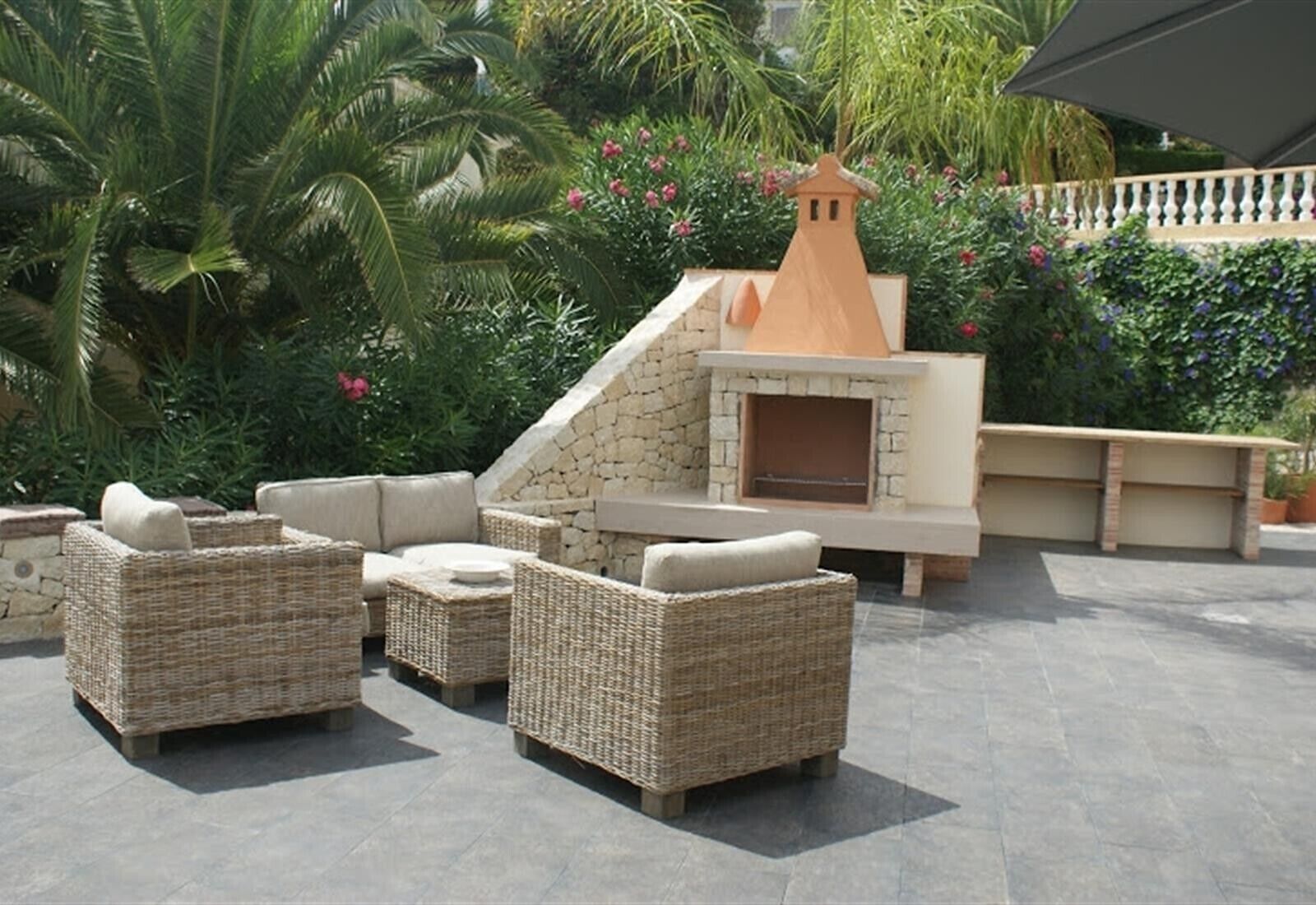 Outdoor wicker furniture, a stone fireplace, and lush greenery.