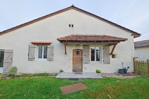 Una casa de un piso con techo a dos aguas, una puerta principal con un pequeño porche y una ventana visible con contraventanas.