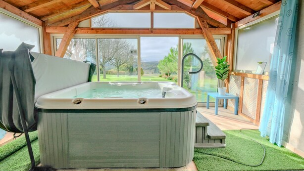 A hot tub in a covered outdoor area with a view of a garden. - Gite Le Moutat-La Cave with Private Garden and Wi-Fi (Allemans)