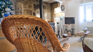 A wicker chair in a room with stone walls, a fireplace, a television, and a Christmas tree. - Gite Le Moutat-La Cave with Private Garden and Wi-Fi (Allemans)