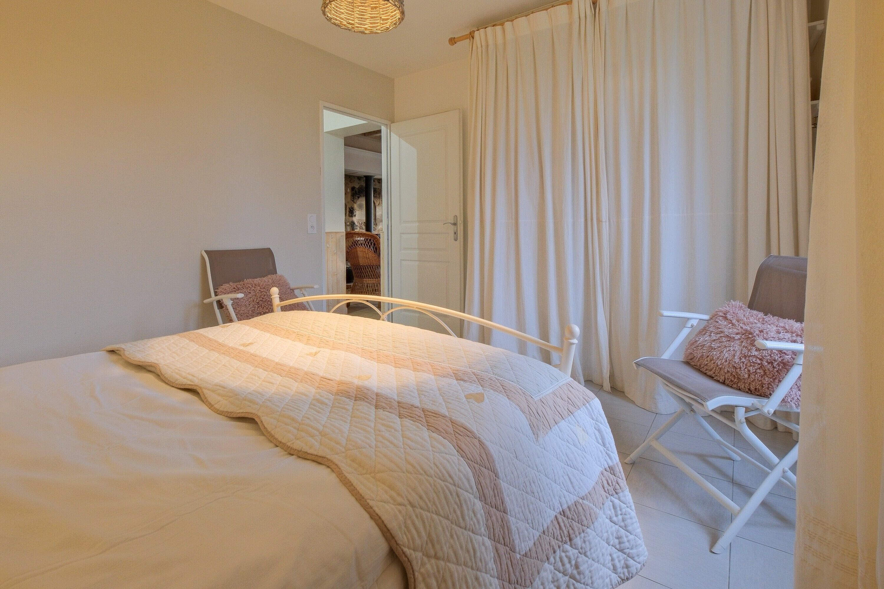 A bedroom with a bed, a chair, a door, and a window with curtains.