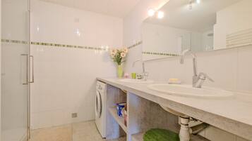A bathroom with a double sink, a mirror, a washing machine, and a green mat on the floor.