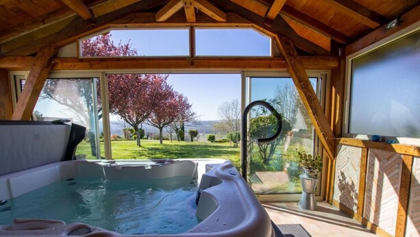 Un jacuzzi en una habitación con ventanas amplias, vigas de madera y vistas a un jardín.