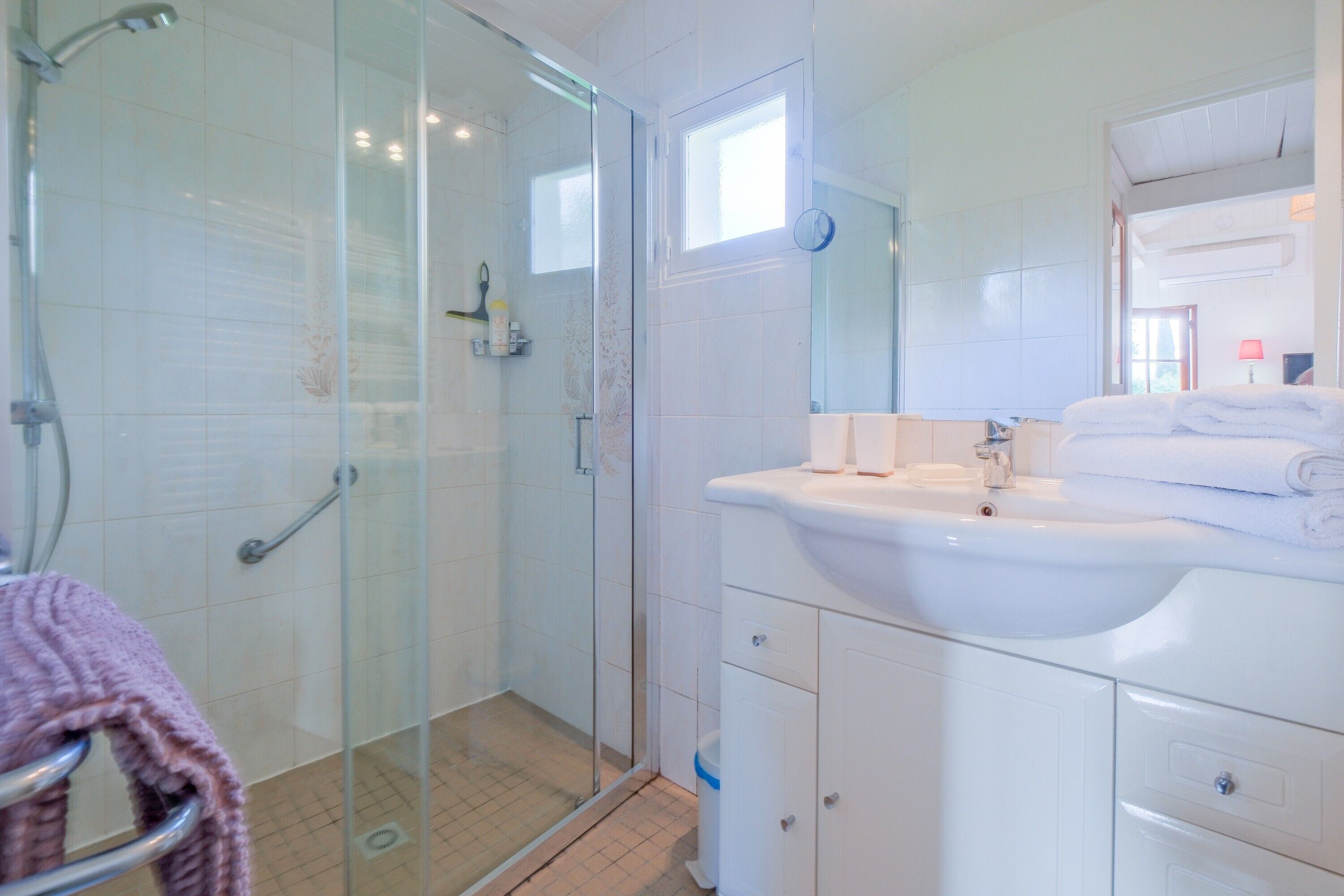 A bathroom with a glass shower enclosure, a white sink, and a mirror.