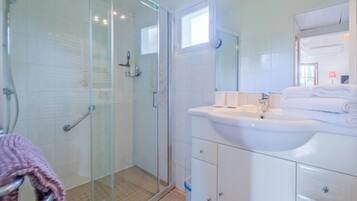 A bathroom with a glass shower enclosure, a white sink, and a mirror.