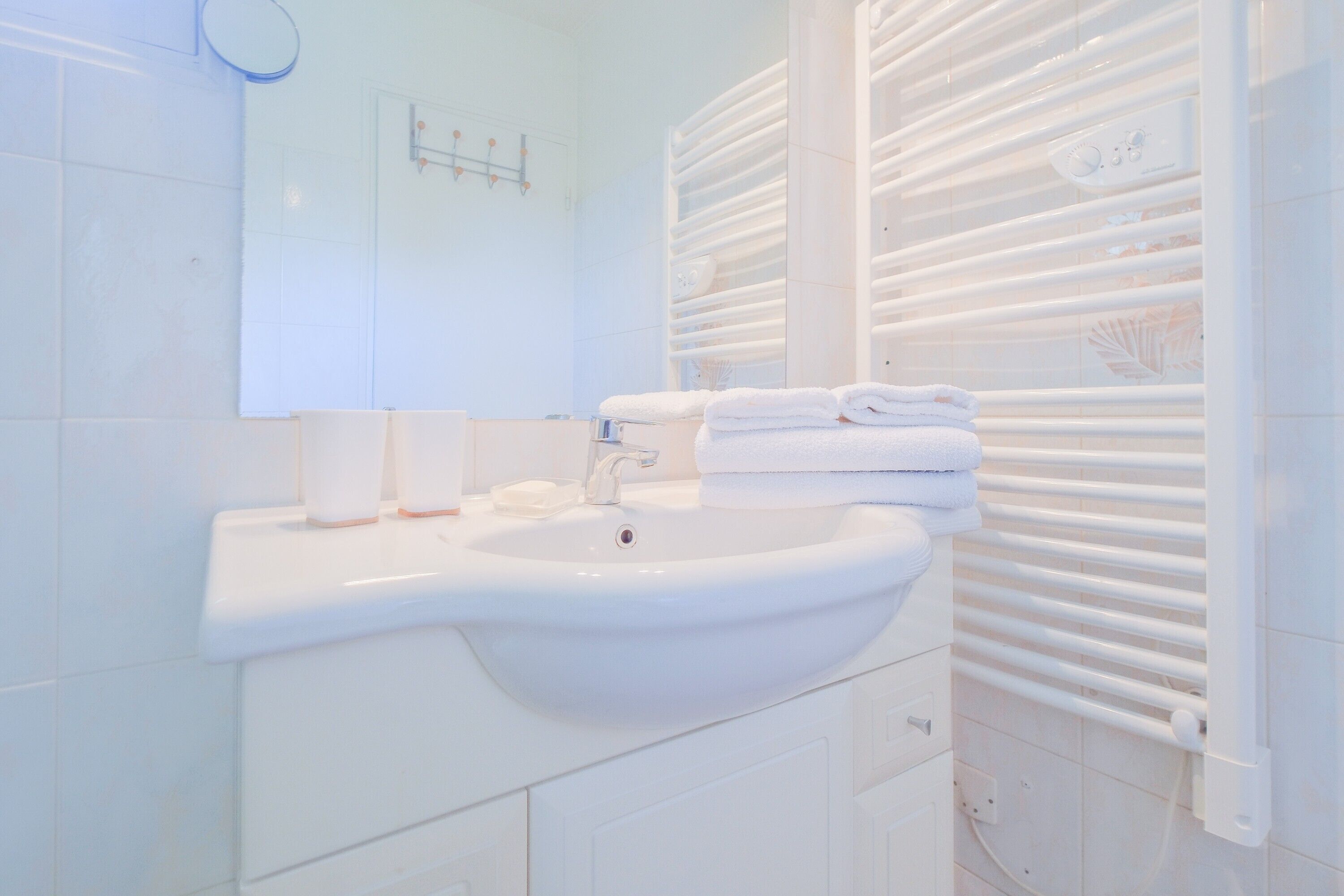 Casa de banho com lavatório branco, espelho e porta-toalhas.