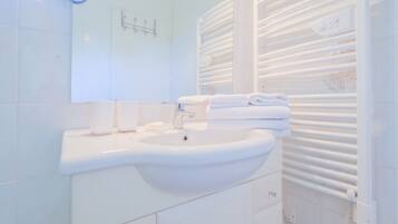 Casa de banho com lavatório branco, espelho e porta-toalhas.