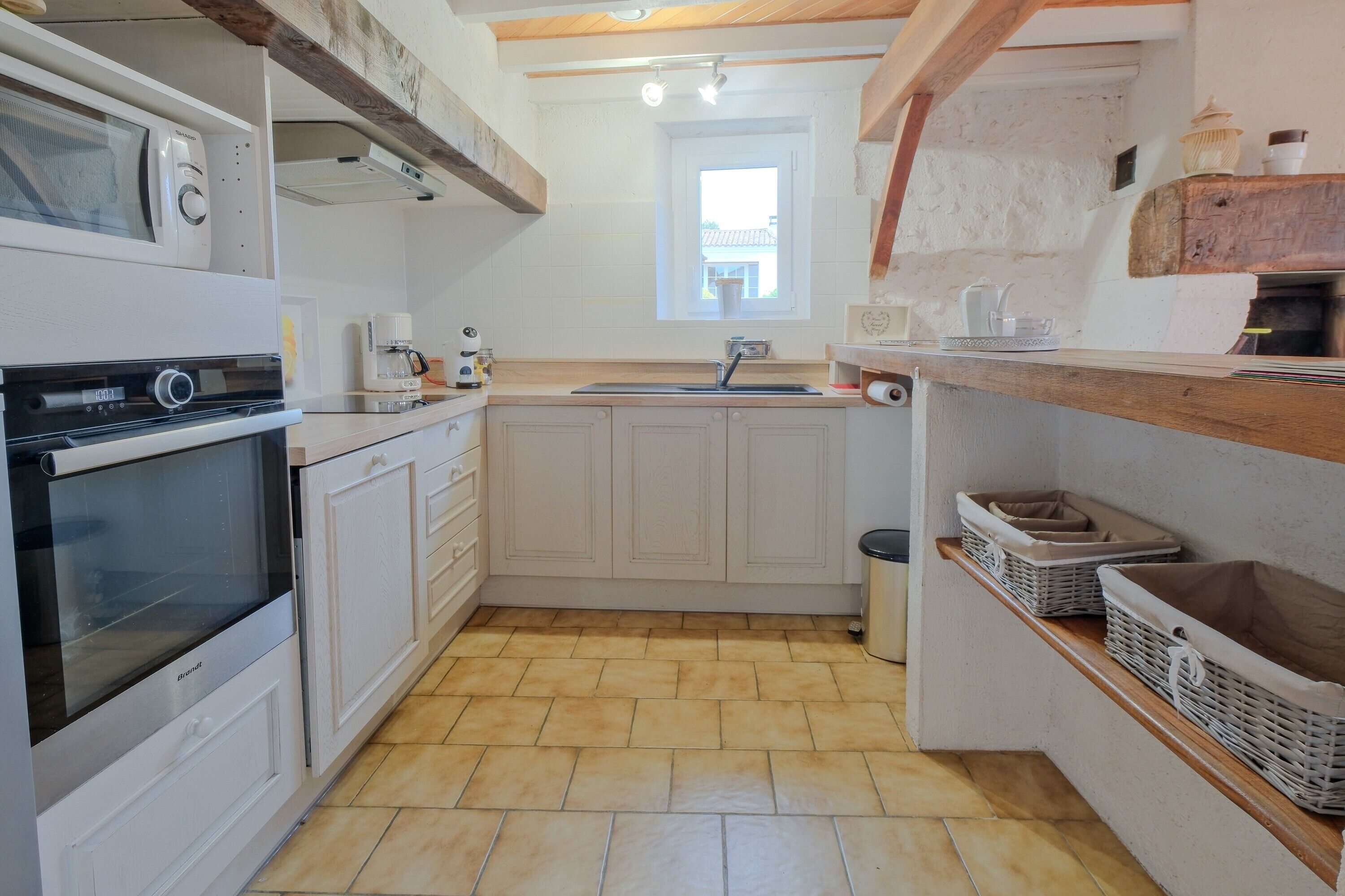 A kitchen with white cabinets, a built-in oven, a sink, and a window.