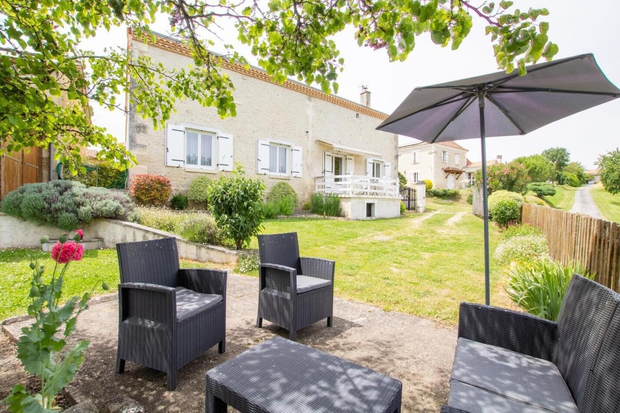 A patio with wicker furniture, a large umbrella, and a view of a house with a balcony.
