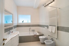 Une salle de bain moderne équipée d’une baignoire, de toilettes, d’un bidet et d’un grand miroir.