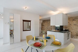 Une cuisine moderne avec un mur en pierre, un meuble blanc et une table à manger décorée de bougies et d’assiettes jaunes.