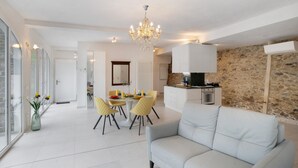 Un salon moderne comprenant un canapé, une table à manger, des chaises, un lustre et un coin cuisine avec un mur en pierre.