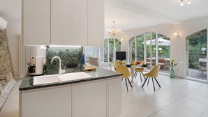 Une cuisine moderne dotée d’un îlot central, d’un coin repas avec des chaises jaunes et de grandes fenêtres offrant une vue sur l’extérieur.