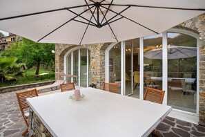 Une terrasse avec une table et des chaises, un grand parasol et un mur en pierre.