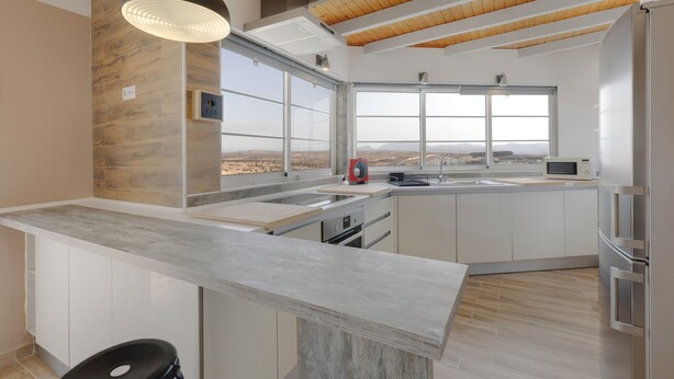 Een moderne keuken met een groot schiereiland, houten balken in het plafond en uitzicht op het landschap.