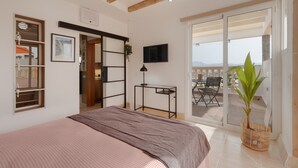 Een slaapkamer met een bed, een bureau, een televisie en een balkon met uitzicht.