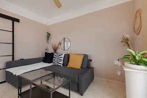 A modern living room with a grey sofa, a glass coffee table, and a potted plant.