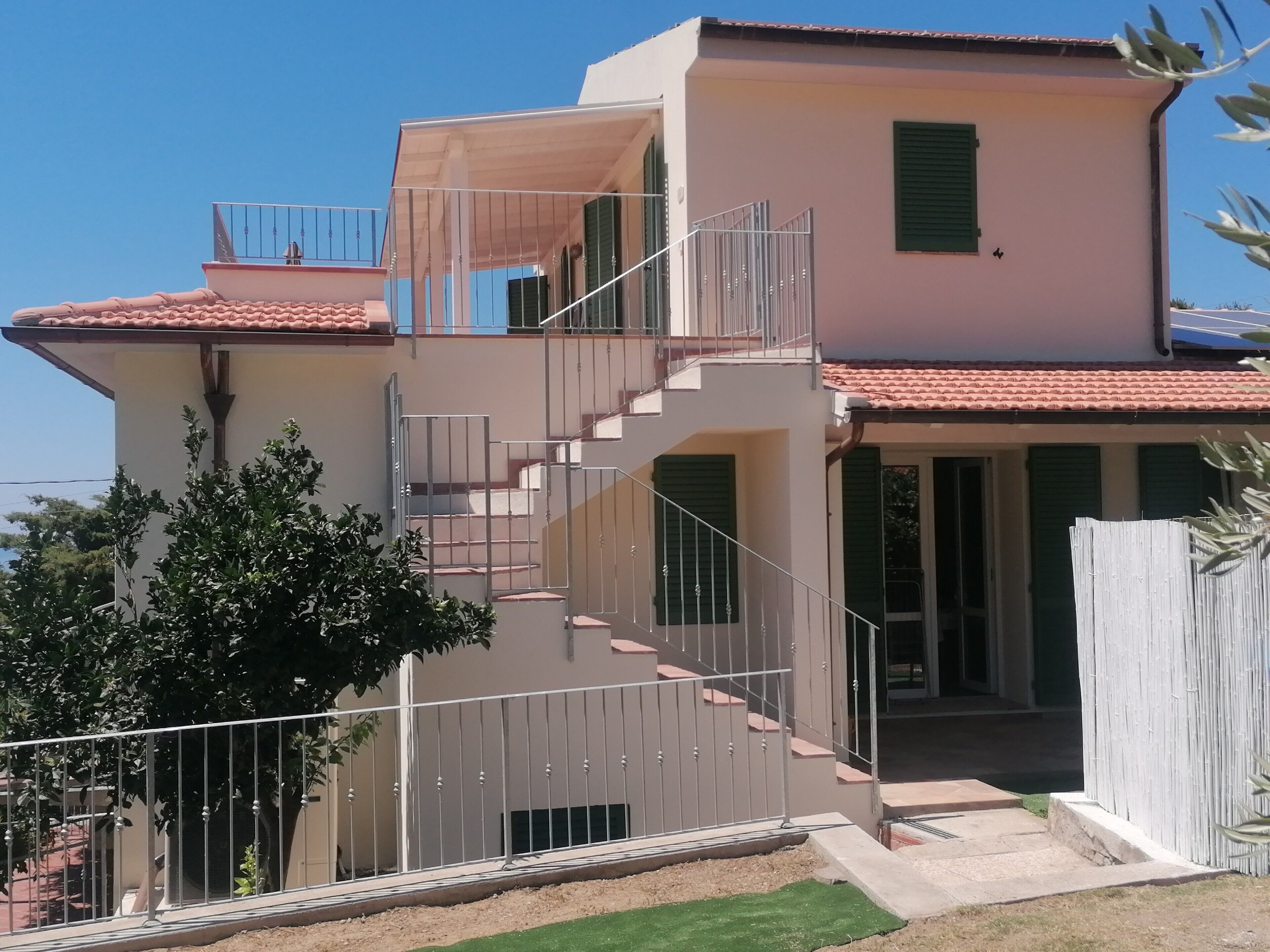 A two-story building with a staircase, a balcony, and a fenced garden area.