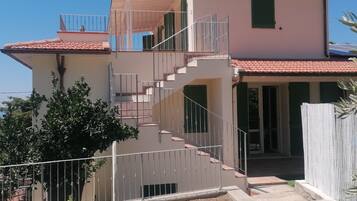 A two-story building with a staircase, a balcony, and a fenced garden area.