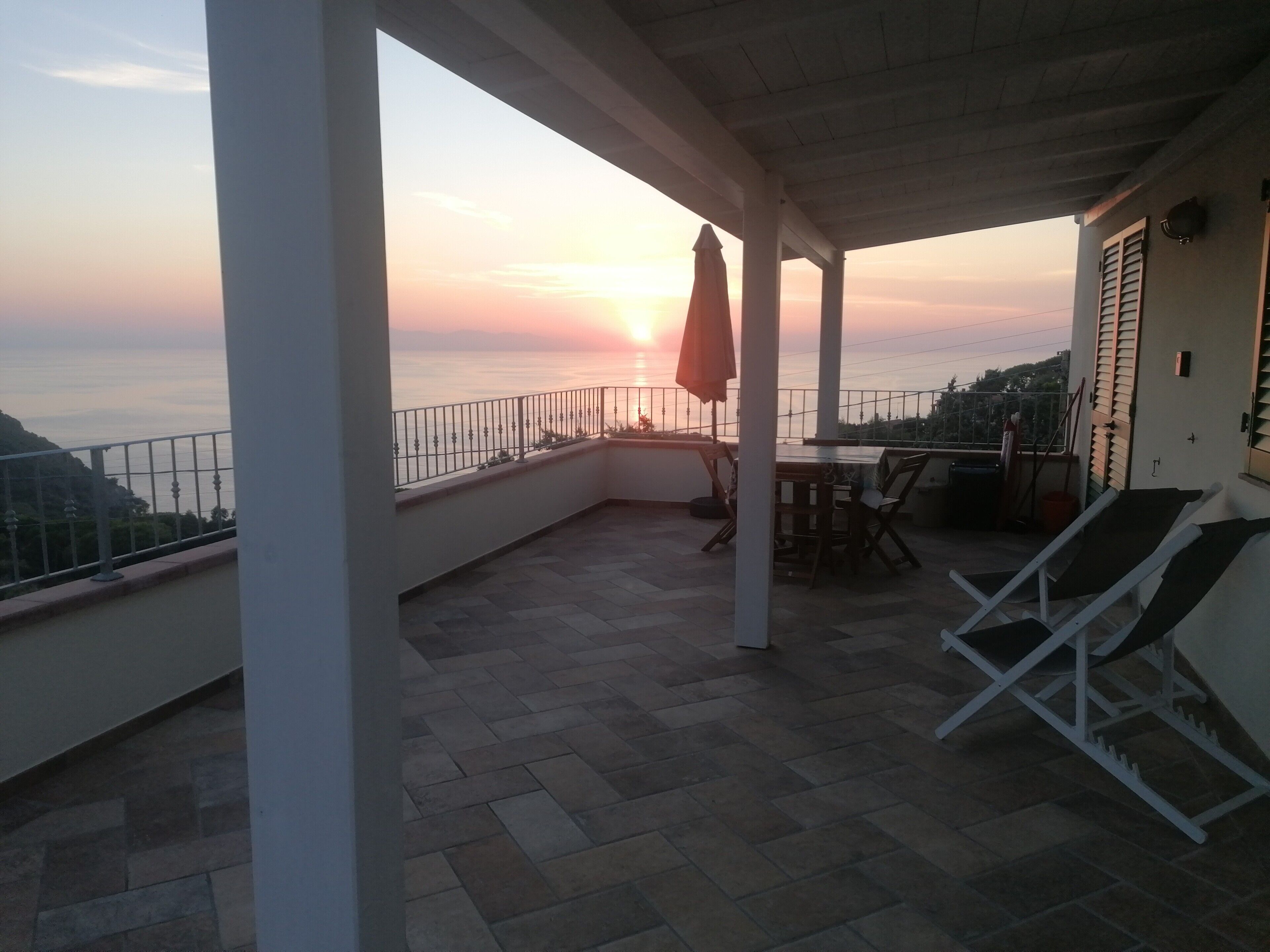 Un balcon avec vue sur le coucher de soleil, une table, des chaises et un parasol.