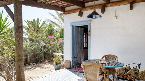 An outdoor patio with a round table and wicker chairs, a wooden pergola, and a white wall with a blue door. - Holiday Home 'Mora' with Private Terrace, Private Garden and Wi-Fi (Vejer de la Frontera)